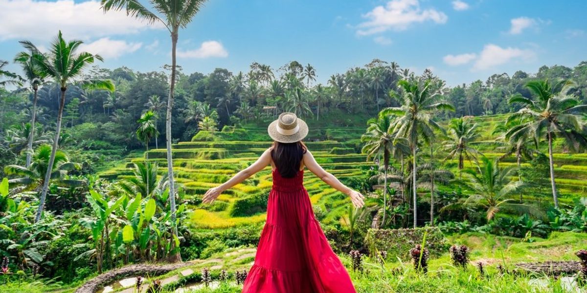 Fiatal nő hosszú szoknyás ruhában, kalapban áll Balin