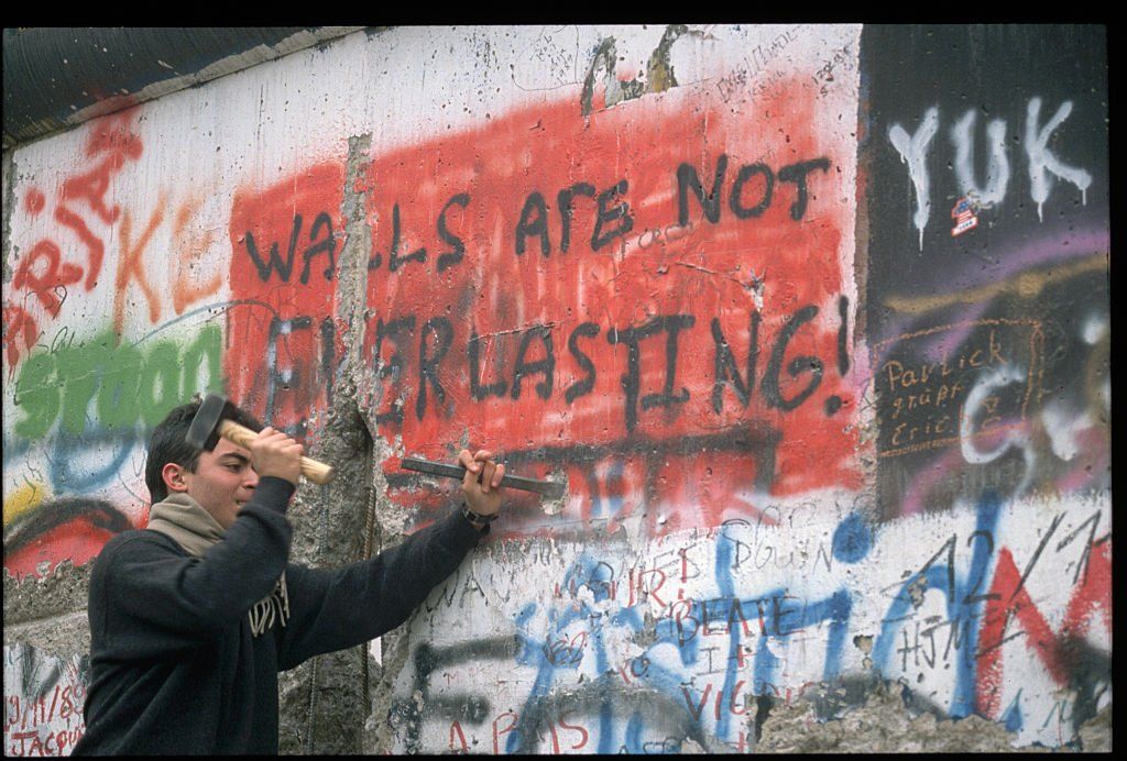 Egy férfi a berlini fal lebontása közben, melyen "A falak nem örökkévalók!" felirat olvasható 