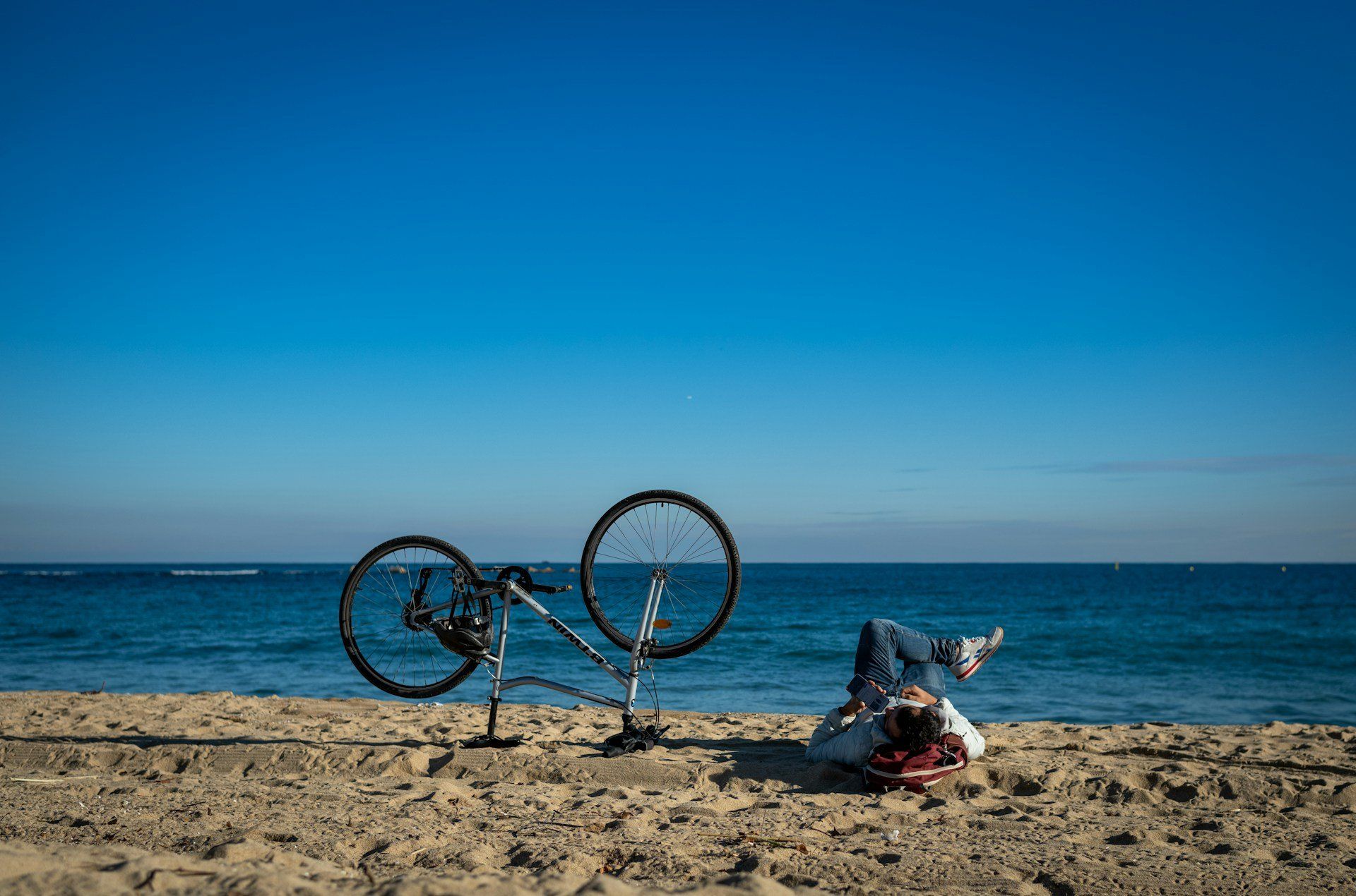 Tengerpartoi homokban fekvő férfi, mellette kerékpár 