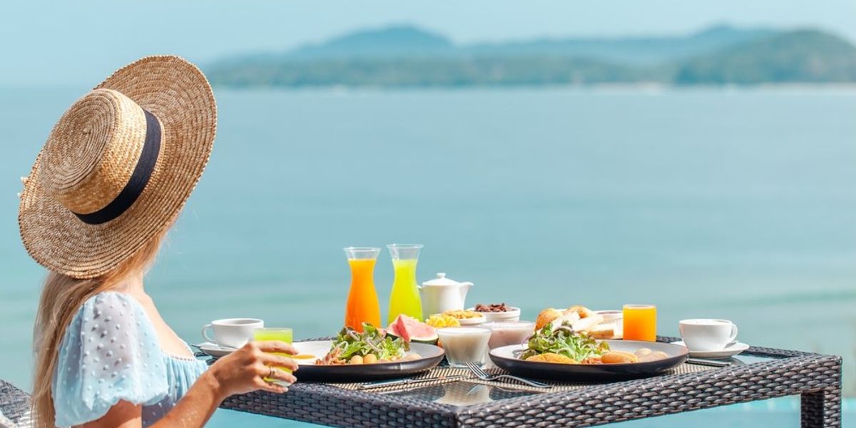 Kalapos fiatal nő a tenger mellett reggelizik