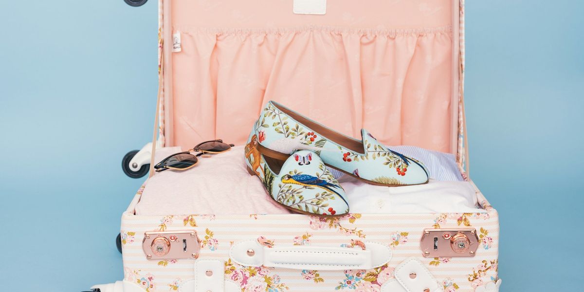 Ruhákkal telepakolt bőrönd, felül napszemüveg és egy pár cipő